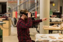 Carpintero masculino usando auriculares de realidad virtual en el taller - foto de stock