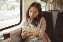Femme utilisant un téléphone portable tout en écoutant de la musique sur un téléphone portable dans le train — Photo de stock
