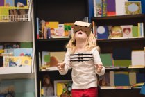 Fille prétendant utiliser casque de réalité virtuelle dans la librairie — Photo de stock