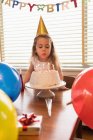 Kleines Mädchen bläst zu Hause die Kerzen auf ihrem Geburtstagskuchen aus — Stockfoto