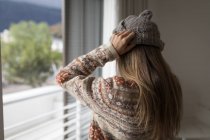 Visão traseira da mulher usando chapéu de lã na sala de estar em casa . — Fotografia de Stock