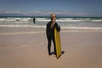 Сидіння в гідрокостюмі, що стоїть з дошкою для серфінгу на пляжі — стокове фото