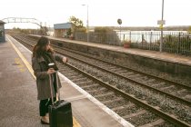 Female executive waiting for train with luggage at railway platform — Stock Photo