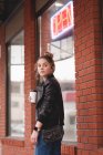 Thoughtful girl standing with disposable glass outside shopping mall — Stock Photo