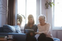 Senior woman and daughter using a tab while siting on the sofa during day time — Stock Photo