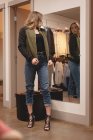 Красивая девушка проверяет куртку перед зеркалом в торговом центре — стоковое фото