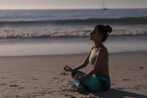 Mujer en forma meditando en la playa de arena al atardecer . - foto de stock