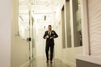 Executivo de negócios olhando para smartwatch enquanto toma café no corredor do escritório — Fotografia de Stock