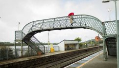 Frau läuft mit Regenschirm auf Brücke am Bahnhof — Stockfoto