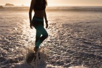Fit femme debout dans éclaboussures d'eau de mer sur la plage au crépuscule . — Photo de stock