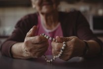 Gros plan de la femme âgée tenant des perles de prière à la maison — Photo de stock