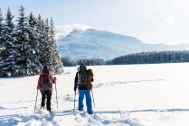 Couple walking together with backpacks in snowy landscape during winter. — Stock Photo