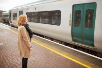 Young woman standing on platform in front of running train on a rainy day — Stock Photo