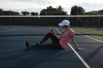 Jeune femme utilisant téléphone portable dans le court de tennis — Photo de stock