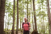 Усміхнена зріла жінка з полюсами, що стоять у лісі — стокове фото