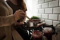 A metà sezione nonna e nipote cucinare marmellata di lamponi in cucina a casa — Foto stock