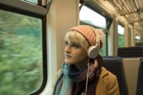 Крупним планом молода жінка в теплому одязі, що спирається на музику на навушники — стокове фото