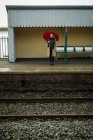 Молода жінка стоїть з парасолькою на залізничному вокзалі — стокове фото