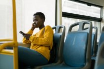 Mujer joven usando el teléfono móvil mientras viaja en autobús - foto de stock