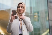 Femme dans le hijab en utilisant le téléphone mobile sur la rue de la ville — Photo de stock