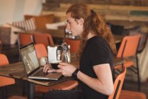Hombre usando el ordenador portátil mientras toma café en la cafetería - foto de stock