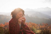 Female hiker in blanket having coffee on a sunny day — Stock Photo