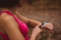 Женщина среднего звена использует умные часы в лесу — стоковое фото