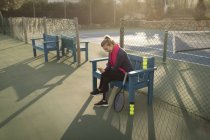 Junge Frau benutzt Handy auf Tennisplatz — Stockfoto