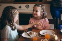 Sisters interacting with each other while having breakfast in kitchen — Stock Photo