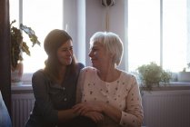 Seniorin und Tochter sitzen auf Sofa und umarmen sich im heimischen Wohnzimmer — Stockfoto