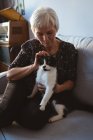 Senior mulher sentada no sofá acariciando seu gato de estimação na sala de estar em casa — Fotografia de Stock