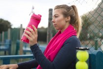 Jovem mulher bebendo água na quadra de tênis — Fotografia de Stock