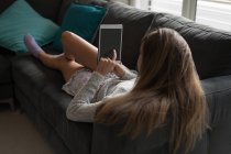Woman using digital tablet on sofa in living room at home. — Stock Photo