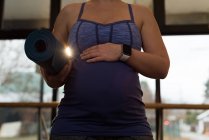 Seção média da mulher grávida segurando um tapete de exercício em casa — Fotografia de Stock