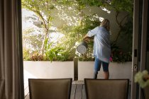 Rückansicht einer Frau mit Beinprothese, die Pflanzen auf der Veranda zu Hause gießt. — Stockfoto