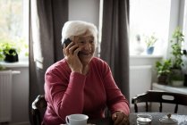 Усміхаючись старший жінка говорити на мобільний телефон у вітальні на дому — стокове фото