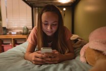 Дівчина лежить на ліжку і використовує мобільний телефон вдома . — стокове фото