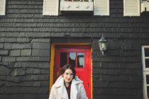 Retrato de mulher em pé na frente da casa com porta vermelha . — Fotografia de Stock