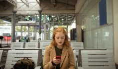 Вид спереду молодої жінки, використовуючи свій мобільний телефон на зупинці автобуса — стокове фото