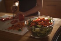 Close-up de tigela de legumes e menina de corte de tomate na cozinha . — Fotografia de Stock