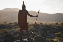 Rückansicht eines Massai-Mannes, der mit Stock auf einem Felsen auf dem Land steht — Stockfoto