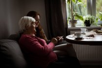 Grandmother and granddaughter looking at photograph in living room — Stock Photo