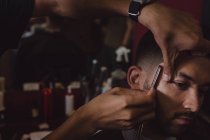 Man getting his hair trimmed with straight razor at barbershop — Stock Photo