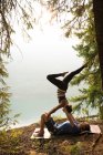 Couple sportif pratiquant l'acro yoga près de la côte par une journée ensoleillée — Photo de stock