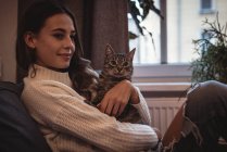 Donna sorridente seduta con il suo gatto domestico a casa — Foto stock