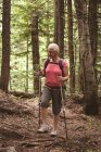 Mulher madura com postes de caminhada em pé na floresta — Fotografia de Stock