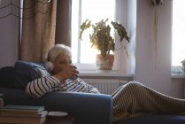 Старша жінка розслабляється на дивані слухаючи музику з чашкою кави у вітальні вдома — стокове фото