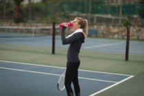 Junge Frau trinkt Wasser auf dem Tennisplatz — Stockfoto