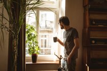 Homem tomando café enquanto através da janela em casa — Fotografia de Stock