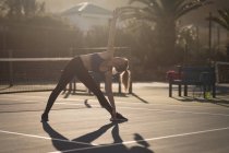 Молодая женщина делает упражнения на растяжку на теннисном корте — стоковое фото